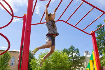 Fototapeta na wymiar Little girl playing on a playground, hanging walk along the monkey bars