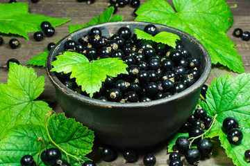 black currants with green leaves in the pottery bowl on a wooden background