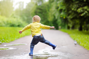 Little boy wearing rain boots jumping in pool of water
