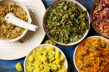 Assortment of dry medicinal herbs in bowls on wooden background top view