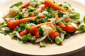 Fresh salad with baby carrots on wooden plate closeup