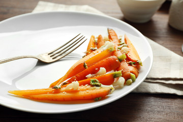 Plate of slices baby carrots with herbs on wooden table closeup