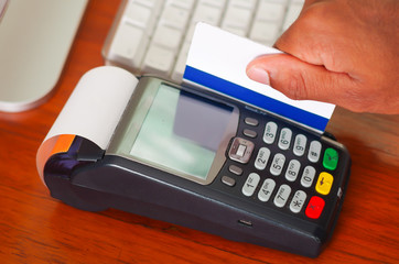 Closeup hand swiping credit card through payment terminal device sitting on wooden surface