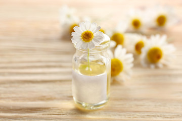 Healing chamomile flower in small glass bottle on light wooden background