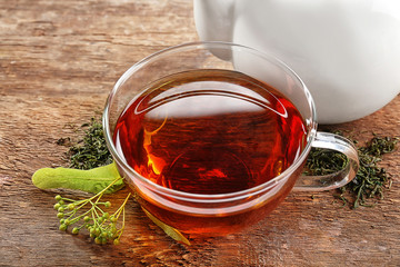 Glass cup of tea with fresh linden and white teapot on wooden background