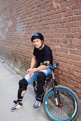 Fototapeta na wymiar Portrait of guy in helmet on a bike sitting against the wall of red brick