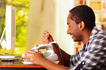 Man standing by desk repairing iron machine using screwdriver, window with garden background