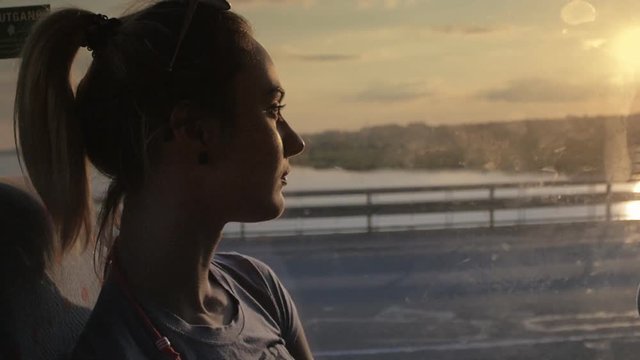 Woman travels in a bus looking out the window at sunset