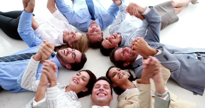 Business people lying in a circle holding hands in the office