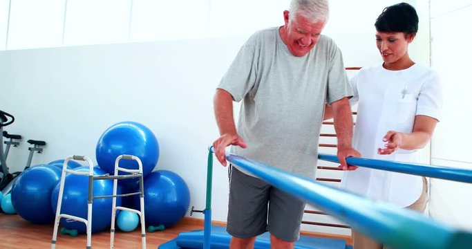 Smiling physiotherapist helping patient walk with parallel bars
