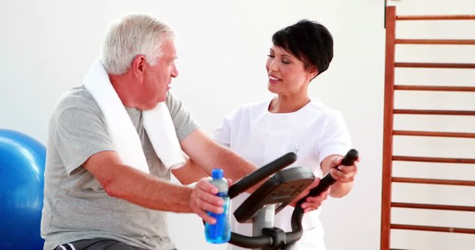 Elderly man using the exercise bike talking to physiotherapist