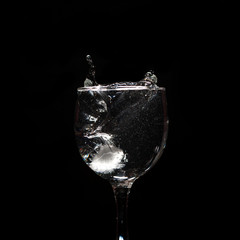 Water splash with ice in glass on black