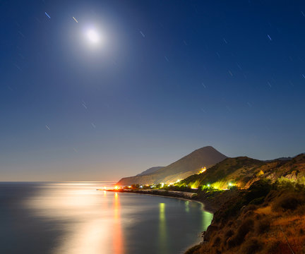 Night landscape with the moon, the sea and the stars in the sky tracks. The village of Mirtos. Crete. Greece