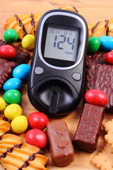 Glucometer with heap of sweets on wooden surface, diabetes and unhealthy food