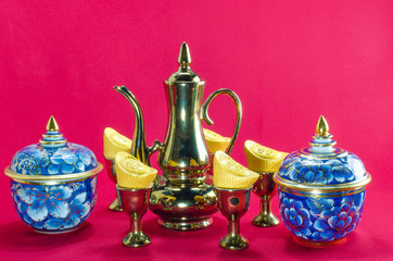 Gold ingot Gold jug Tea glass benjarong  on red background.