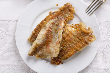 Fried rose fish fillet on a white plate.