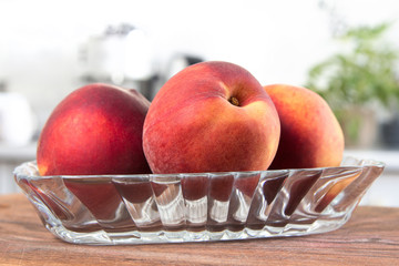 Few peaches on glass pale. White modern kitchen at the background