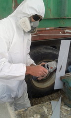 Worker in protective white suit and mask cutting fiber glass with grinder	