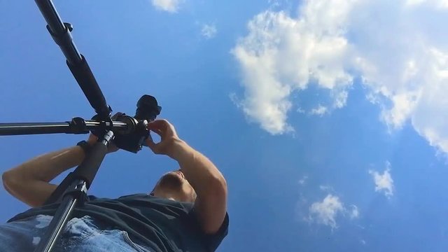 Young videographer on the camera's shooting landscapes. Tsyfrovaya the camera is on a tripod. A view of the sky with clouds prletayuschimi over man. Timelapse video operator Jobs