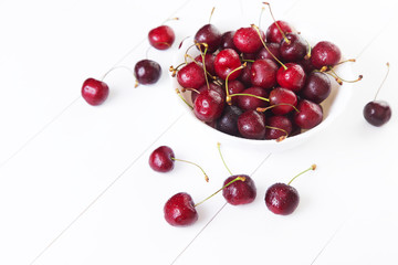 Naklejka na ściany i meble Red cherries with water drops in bowl on a white background. Space for text