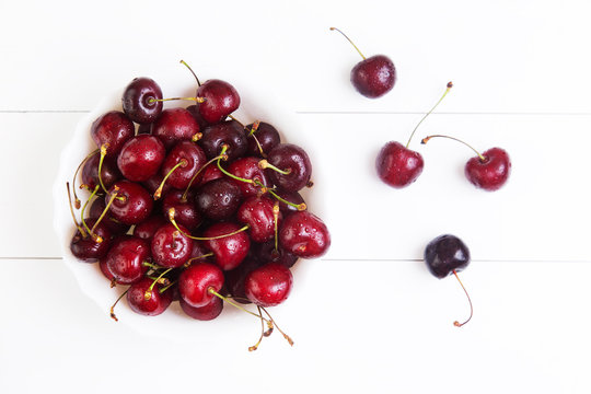 Ripe red cherries with water drops in bowl on a white table