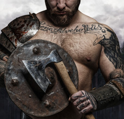 Cropped tattooed male's body with axe and shield.