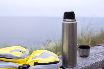 Thermos and yellow bag on wooden bench  background of the sea