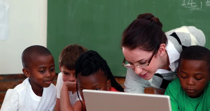 Pupils and teacher looking at laptop in classroom in elementary school