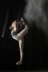 Plakat Gymnastic flexible woman standing on equilibr stand while sprinkled flour