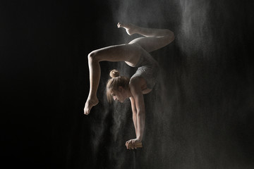 Obraz na płótnie Canvas Gymnastic flexible woman handstand on equilibr at sprinkled flour