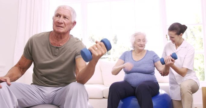 Smiling nurse helping senior couple doing exercises