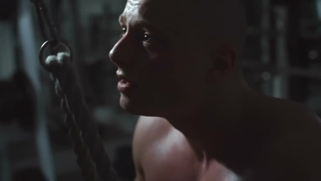 Young sportsman pulling down cable of crossover machine while training in the gym