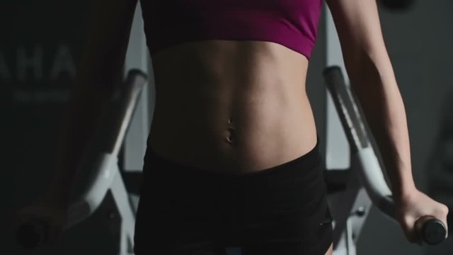 Close up of woman lifting her body up and down on parallel bars in the gym