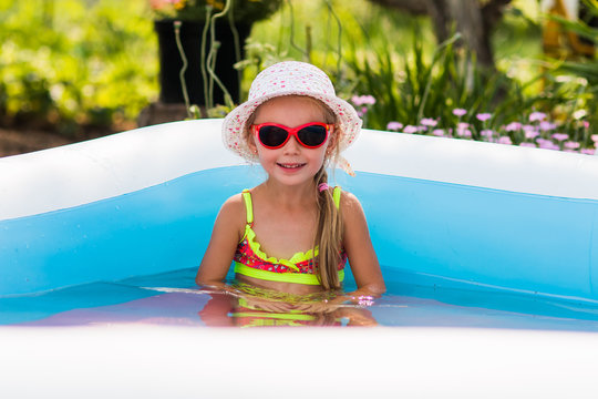 girl with a hat, sunglasses and bikini relaxing in a pool in the garden on a warm summer day