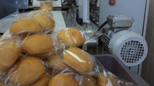 Freshly baked rolls are packed in transparent film, formed a mountain on a conveyor belt.