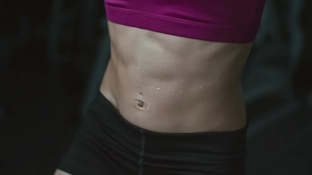 Midsection of woman with perfect abs hanging on pullup bar and doing crunches with knee raise