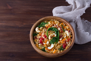 Indian rice with spinach and cashew nuts in a wooden bowl on a dark wooden table