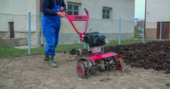A man is fixing a cultivator for plowing the garden. He will now starting to turn over the soil. Wide-angle shot.
