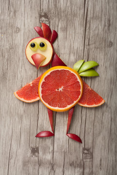 Funny chicken made of fruits on wooden background