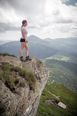 Girl hiker standing on cliff and looking at the mountains.