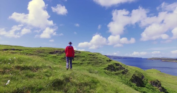 A female hiker walking through a sunny green meadow on the cost near Dunvegan on the Isle of Skye, Scottish Highlands.UK.