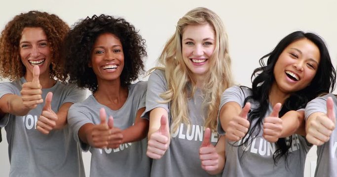 Happy female volunteers showing thumbs up in white room