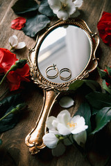 Beautiful wedding rings on a vintage mirror with flowers
