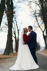 Naklejka premium Gorgeous wedding couple stands on the road covered with golden l