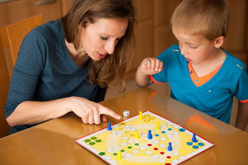 young boy plays ludo game with his mother on a table in livingro