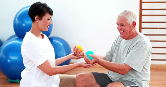 Smiling physiotherapist squeezing massage balls with patient