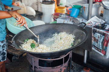 Woman cooks stir-fried noodles with bean sprouts