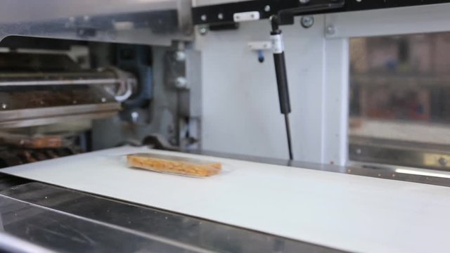On conveyor pieces of bread packed in transparent packaging.