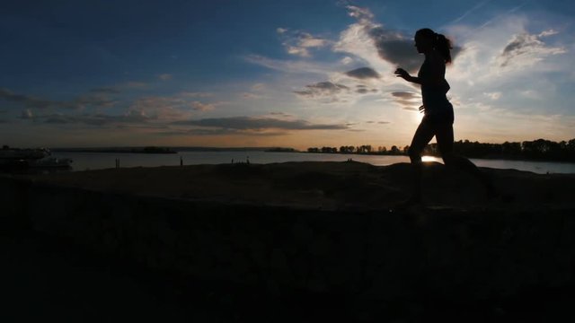 Running young woman with curly hair in park at sunset, slow-motion, silhouette