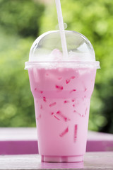 Iced pink milk in plastic glass. Natural garden background.